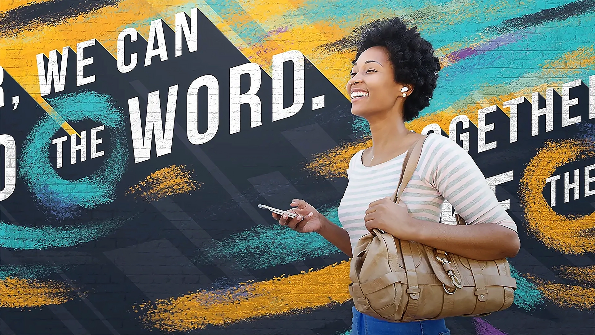 A smiling woman with curly hair walks while holding a phone and beige handbag. She is in front of a vibrant mural with colorful streaks, featuring the text "TOGETHER, WE CAN SPREAD THE WORD," capturing the spirit of the DefeatDD Event beautifully.