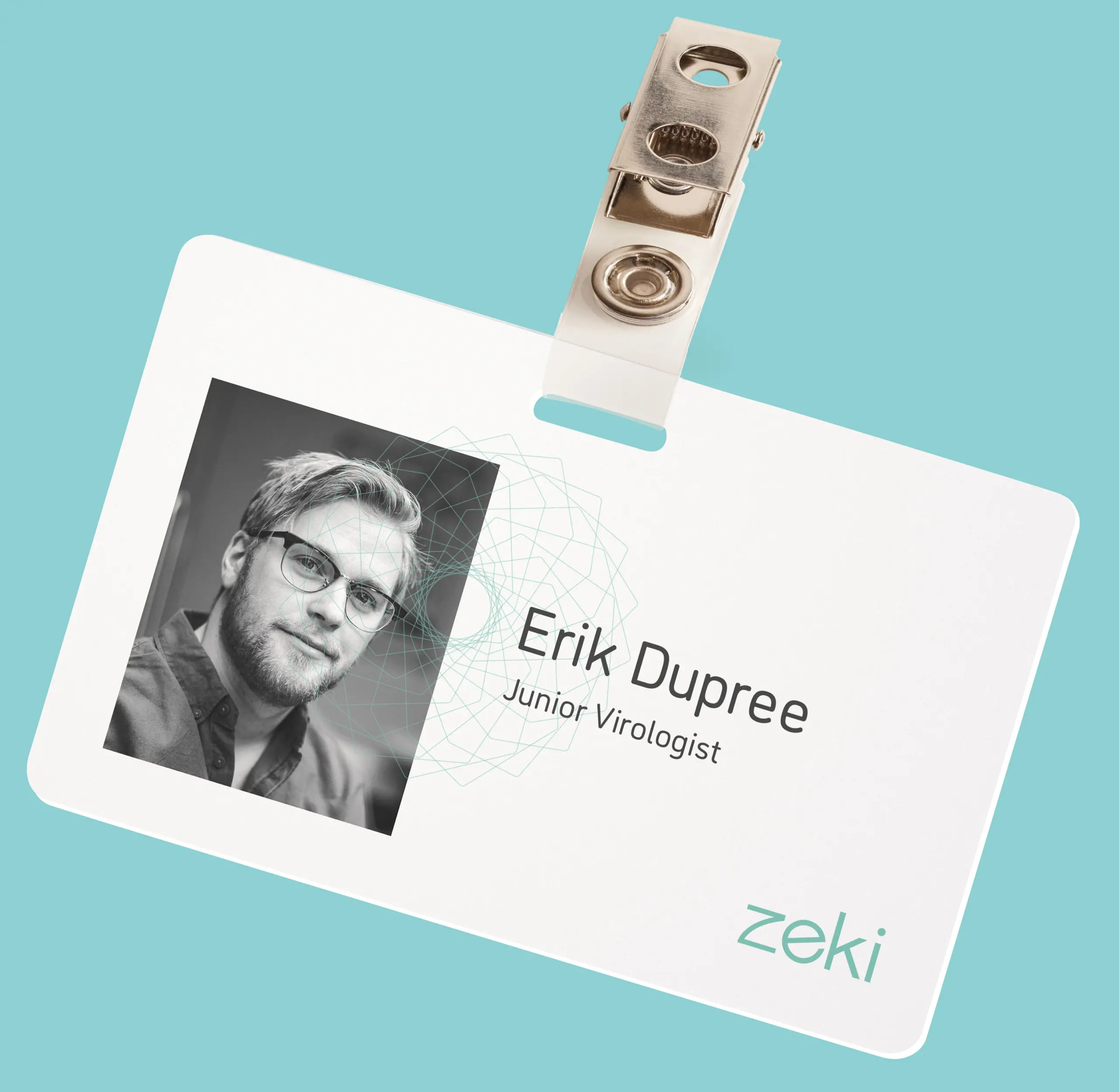 A white identification badge reads "Erik Dupree, Junior Virologist" in black text. The badge has a portrait of a bearded man wearing glasses on the left side. A metal clip is attached to the top of the badge, and the logo "zeki" is printed at the bottom right.