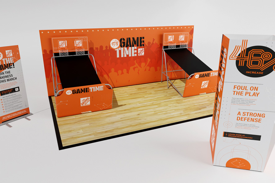 An indoor basketball game setup with two hoops against an orange backdrop that reads "IT'S GAME TIME". The foreground has a large sign featuring the number 46, the text "FOUL ON THE PLAY" and "A STRONG DEFENSE". Another smaller sign is partially visible.