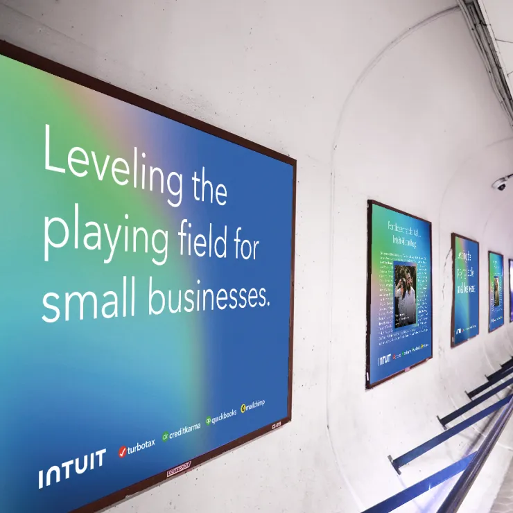 A series of Intuit ads are displayed in a curved, underground metro tunnel. The main ad reads, "Leveling the playing field for small businesses." Intuit's logo and product names—TurboTax, Credit Karma, QuickBooks, and Mailchimp—are featured at the bottom.