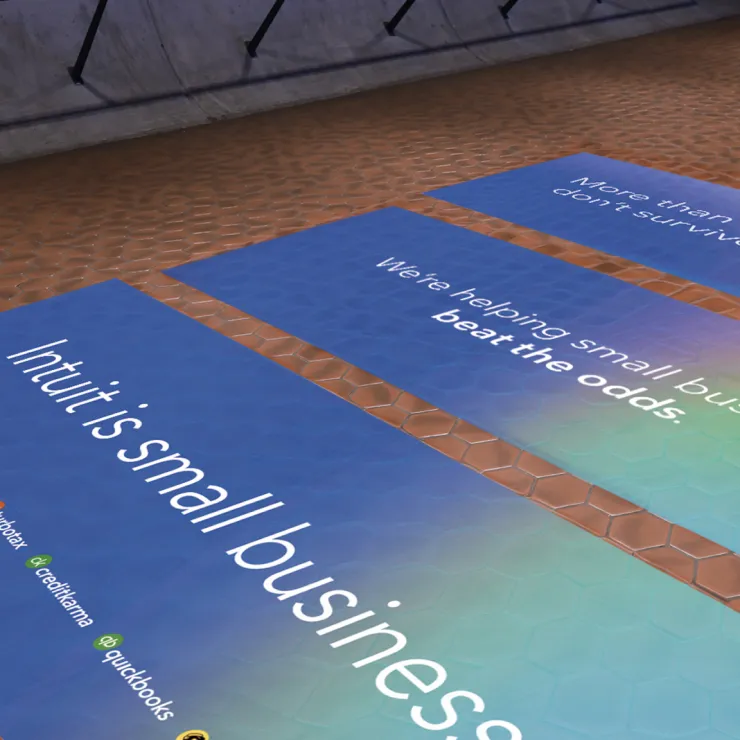 A textured floor with blue banners displaying business-related text. Prominent phrases include "Intuit is small business," "We’re helping small businesses beat the odds," and mentions of various Intuit services like Mailchimp, Credit Karma, and QuickBooks.