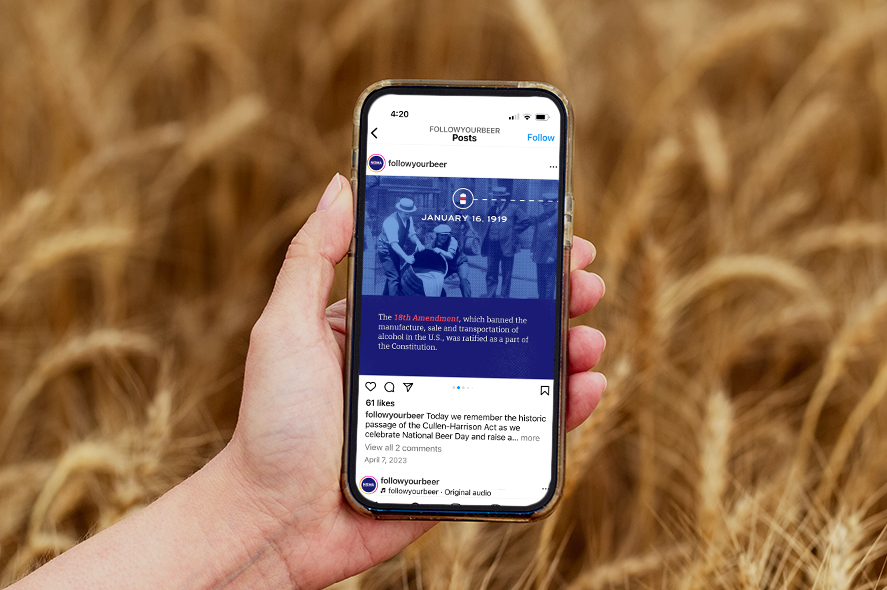 A hand holding a smartphone in a wheat field. The phone screen shows an Instagram post from the account "followyourbeer" celebrating the ratification of the 18th Amendment, which enacted alcohol prohibition in the USA on January 16, 1919.