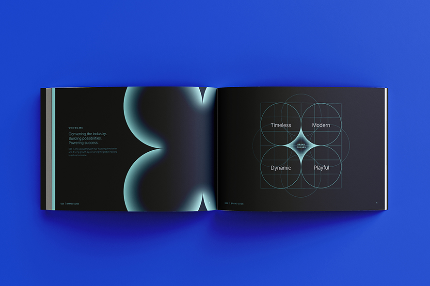 An open book on a blue surface shows a visual graphic spanning two pages. The left page has a glowing abstract shape with a cyan gradient and text that reads "Conveying the industry. Building possibilities. Redefining sections." The right page has overlapping circles labeled "Timeless," "Modern," "Dynamic," and "Playful.