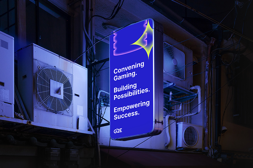 A glowing vertical sign in an urban alley reads: "Convening Gaming. Building Possibilities. Empowering Success." The sign features a stylized bird icon and the G2E logo at the bottom. Surrounding the sign are various air conditioning units mounted on the wall.