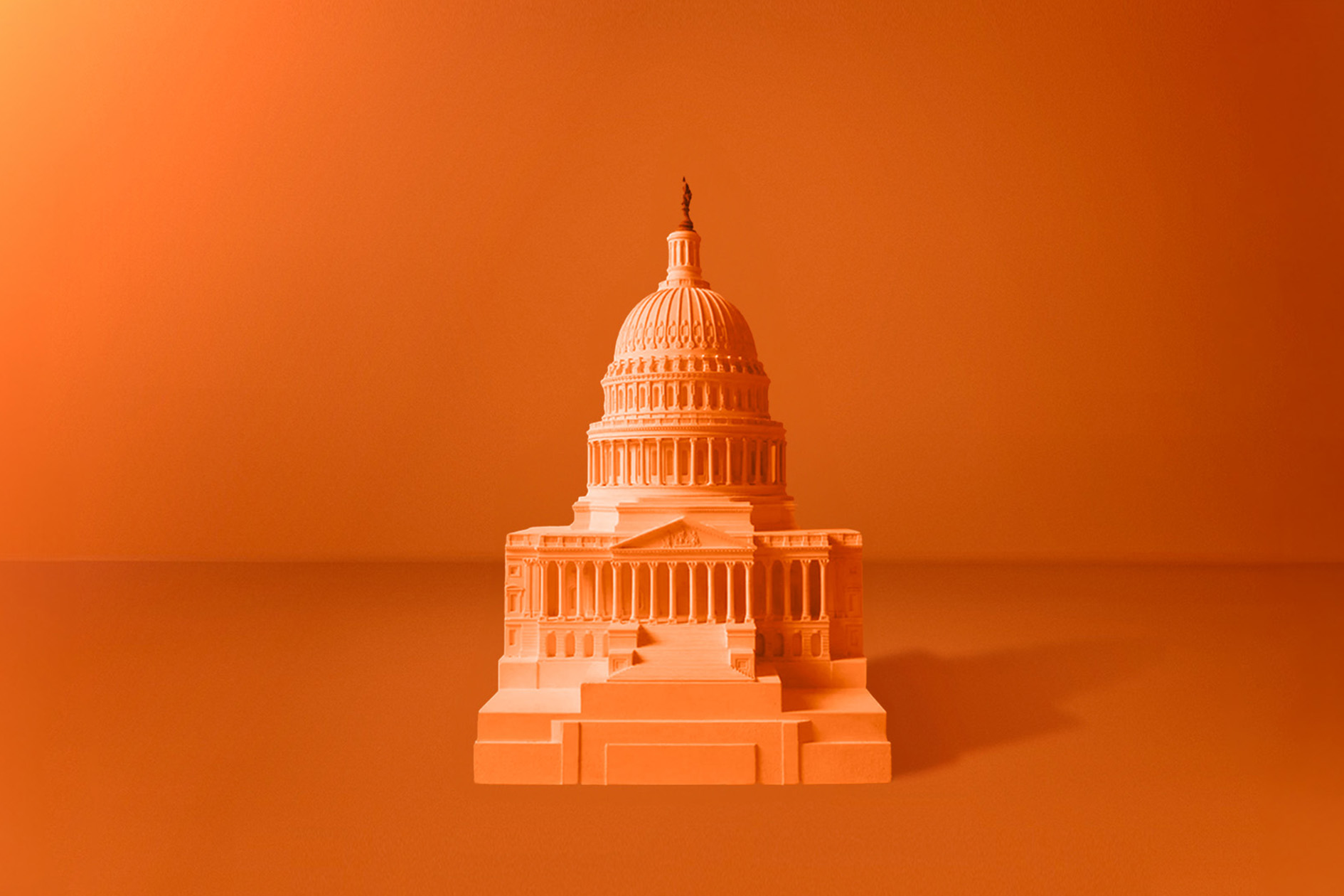 A miniature model of the United States Capitol building is set against a monochromatic orange background. The detailed architecture of the dome and surrounding structures is highlighted, creating a striking visual contrast with the uniform backdrop.