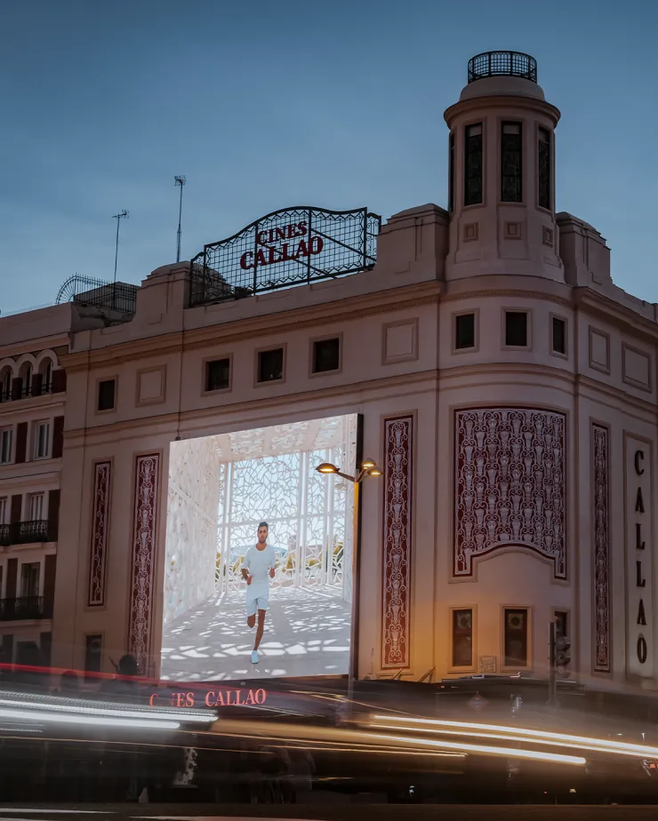 A historic building with the sign "Cines Callao" prominently displayed at the top. A large, illuminated digital screen on the building shows a woman in a white outfit walking in a bright, architectural space. Blurred car lights streak in the foreground.