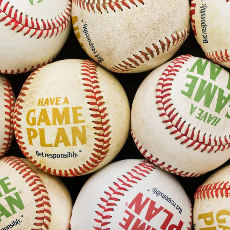 A close-up shot of multiple baseballs, some of which are labeled with the message "HAVE A GAME PLAN, Bet responsibly" in various colors like green, yellow, and red. The baseballs are arranged in a random pile.