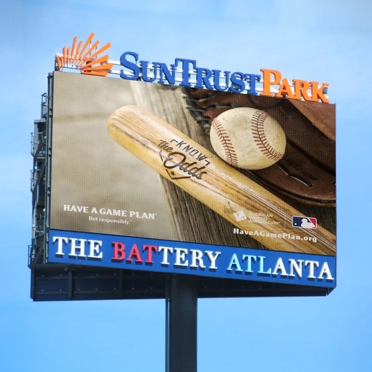 A large billboard outside SunTrust Park in Atlanta shows an image of a baseball bat and a ball with the text "Know The Odds" and "Have a Game Plan." The billboard also promotes responsible behavior and provides a website URL: HaveAGamePlan.org.