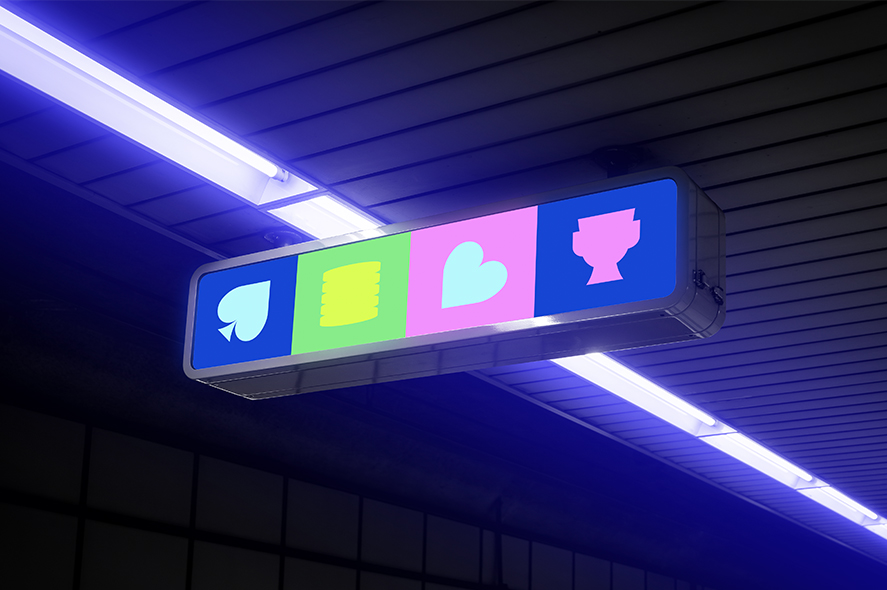 A brightly lit rectangular sign hangs from the ceiling, featuring four icons: a blue spade, yellow poker chips, a pink heart, and a blue trophy. The background above the sign is a ceiling with blue fluorescent lights.