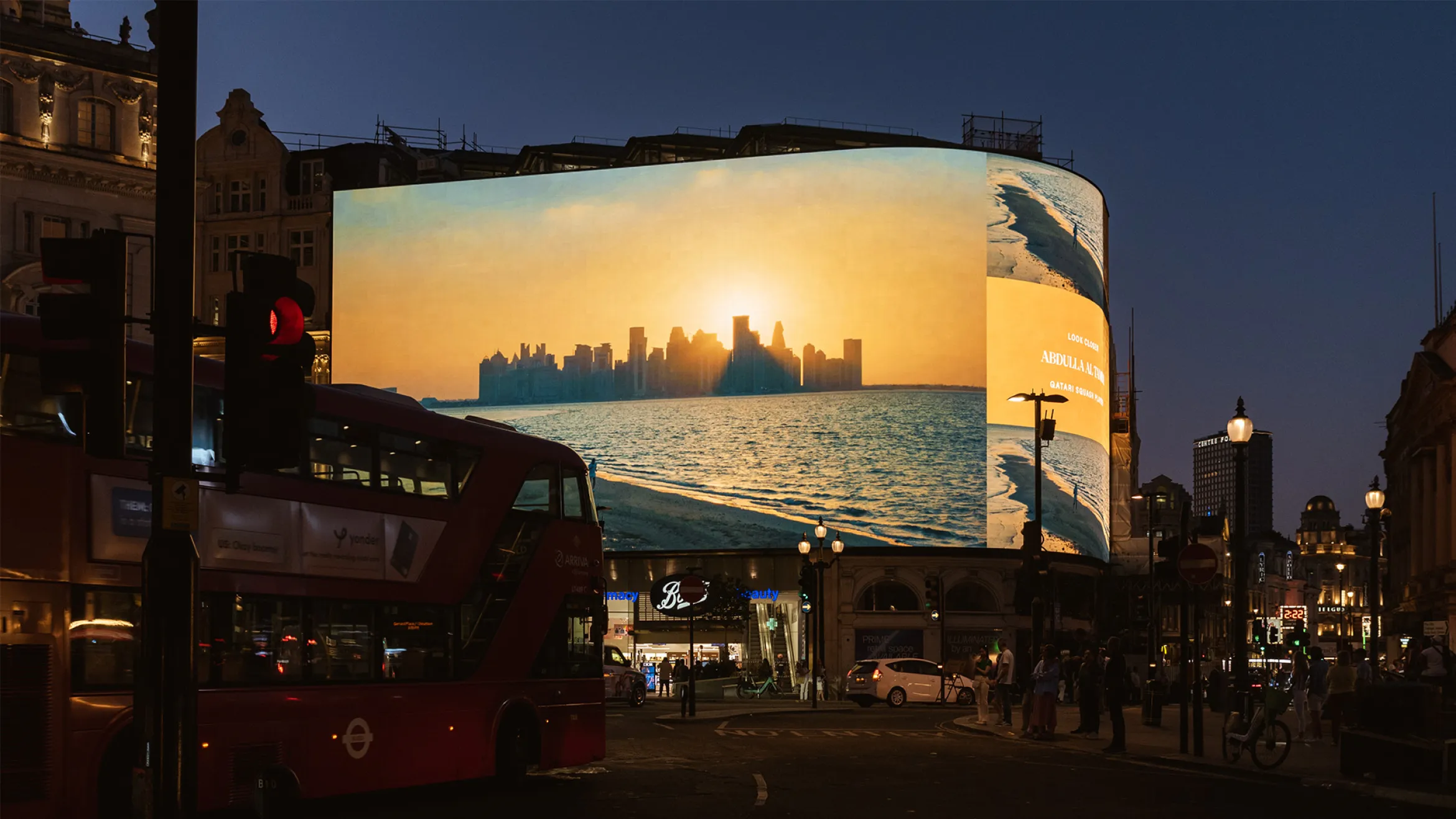 A large digital screen at Piccadilly Circus in London displays an advertisement featuring a city skyline at sunset over water. A red double-decker bus is passing by, and surrounding buildings are illuminated as evening falls.