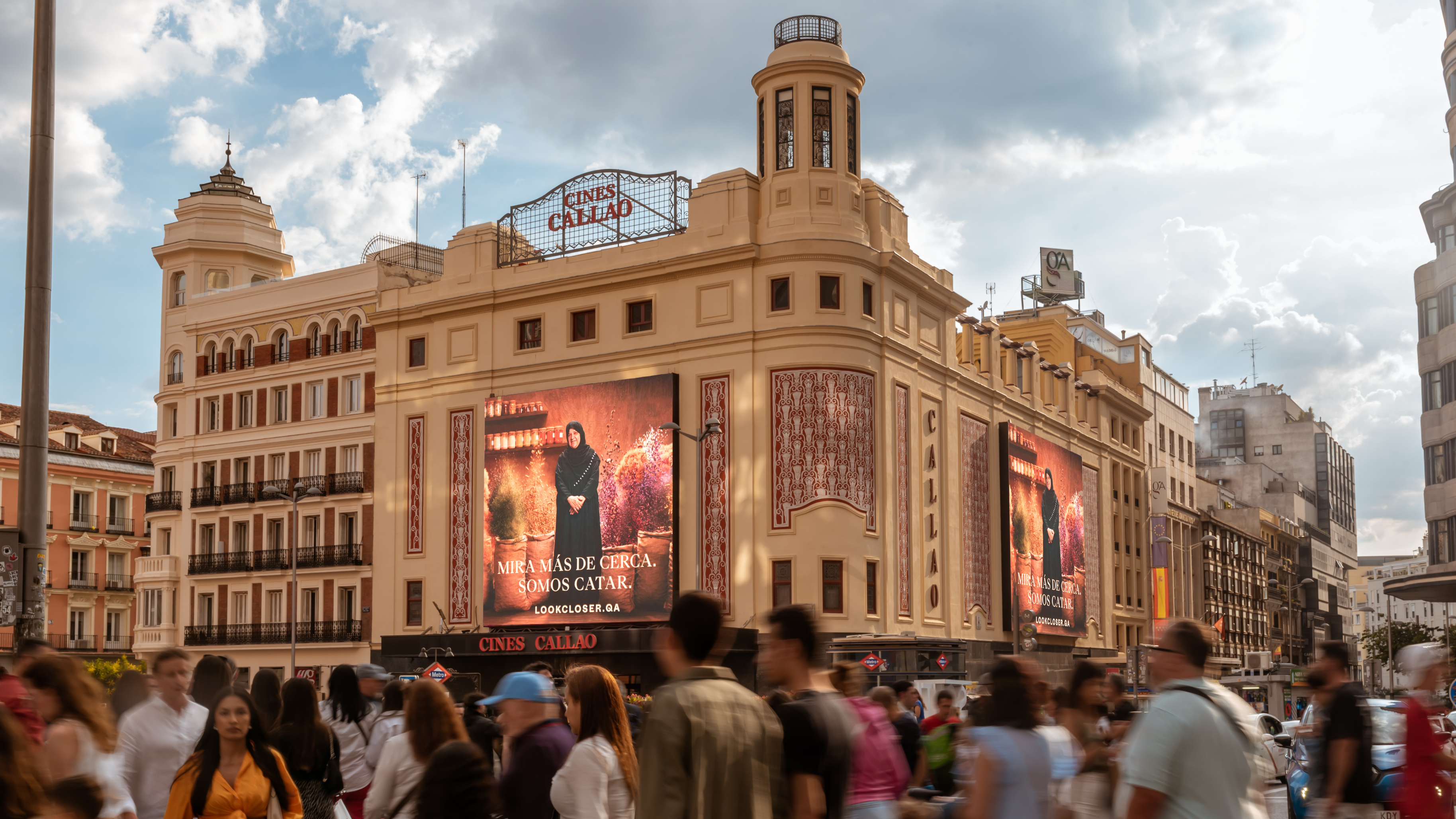 A bustling city scene unfolds as a symbol of nation branding, with many people walking past a historic cinema building. The ornate architecture and large digital screens displaying vibrant advertisements stand proudly against the partly cloudy sky, adding a dynamic backdrop to the urban setting.