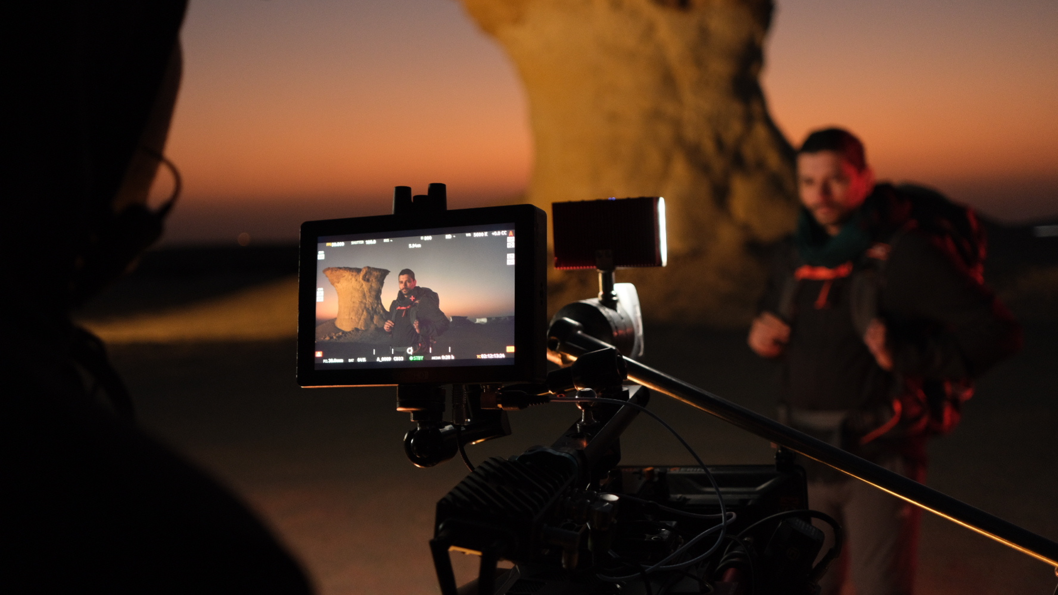 A camera setup captures a scene at sunset, vividly showcasing a person with a backpack in focus on the monitor. This picturesque moment ties into nation branding as the background features an iconic rock formation against a colorful sky, embodying the country's natural allure.