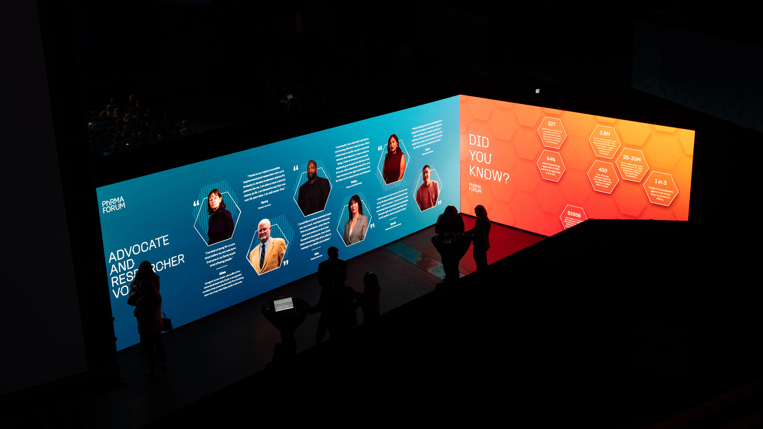 Silhouettes of people stand before large illuminated panels. The left panel is blue, showcasing portraits and text on health communication, while the right panel glows orange with hexagonal shapes and "Did You Know?" text, sparking curiosity in public policy communications.