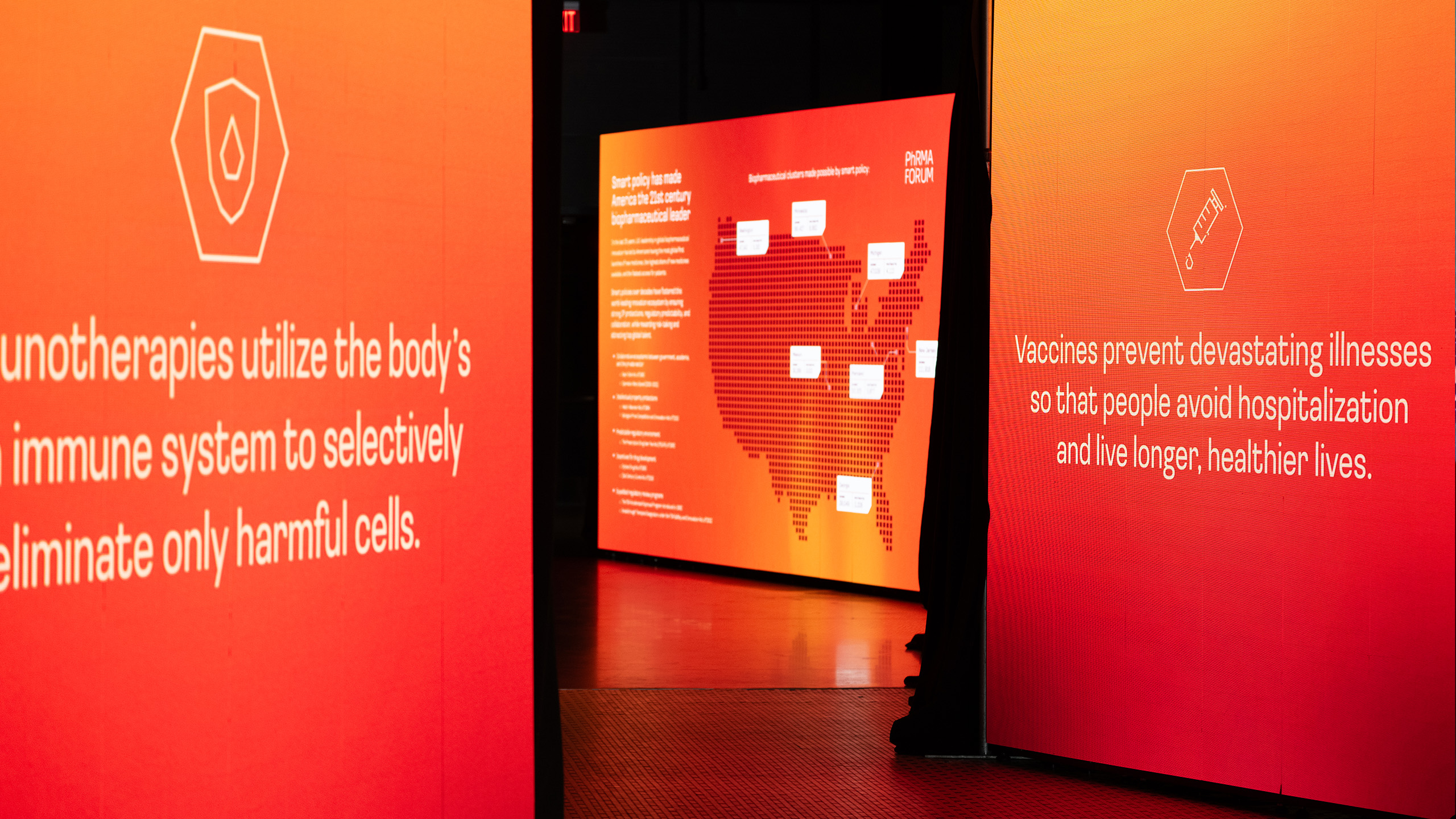 Bright orange display panels with white text about immunotherapies and vaccines form a striking digital campaign. One panel features a map of the United States with highlighted areas, emphasizing PhRMA's dedication to health benefits and illness prevention through strategic communication.